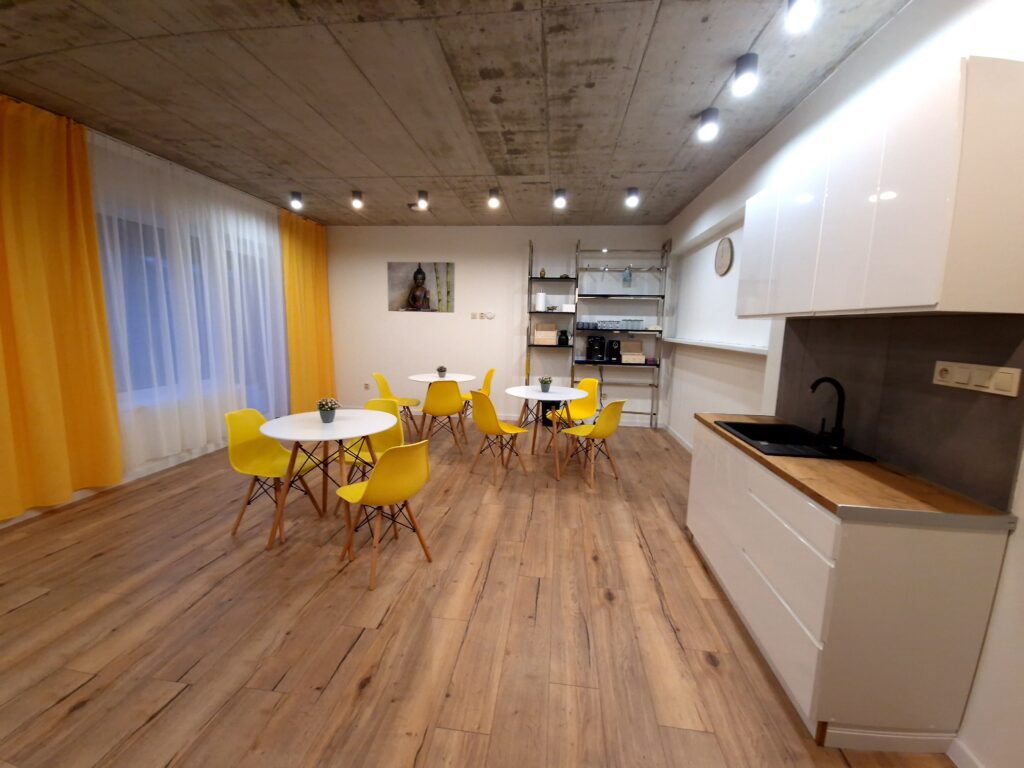 Interiér kuchyne v apartmánoch Birdhouse s tromi stolmi, deviatimi stoličkami, umývadlom vpravo a obrazom na stene